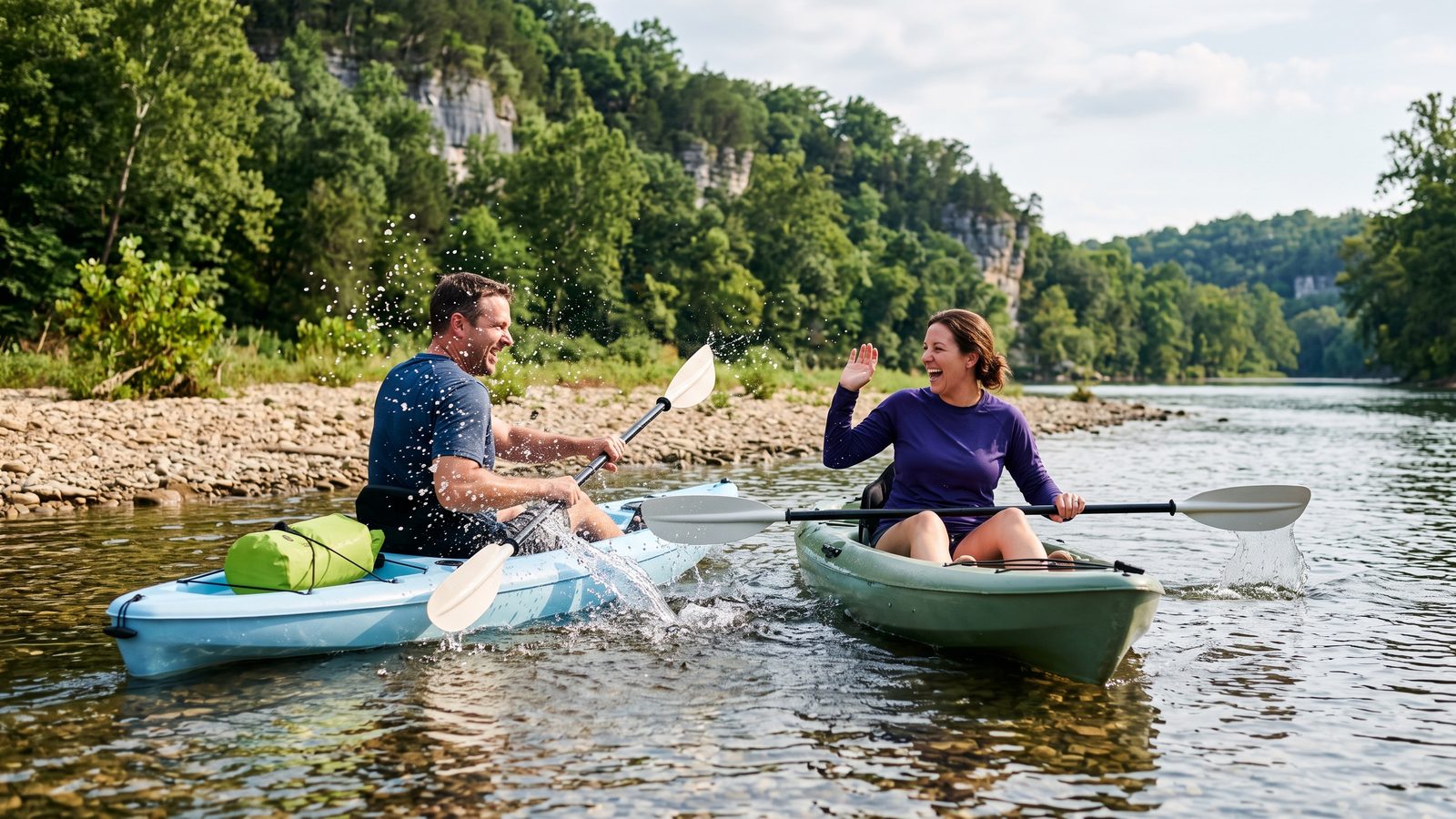 A laughing man and woman paddle two kayaks through clear, shallow water on a river lined with wooded limestone bluffs.
